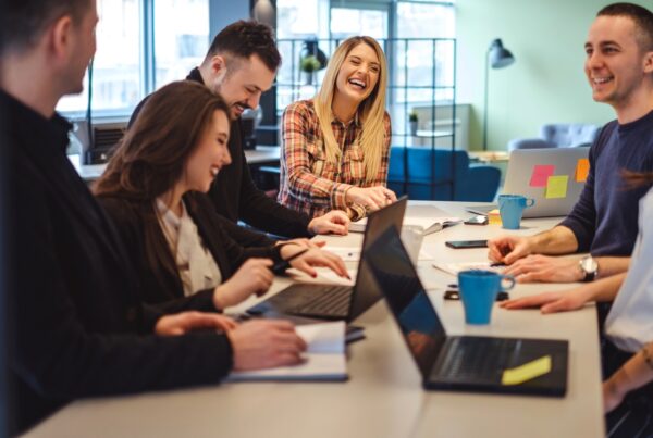A diverse group of people sitting around a table with laptops, collaborating and working together in an indoor office setting.